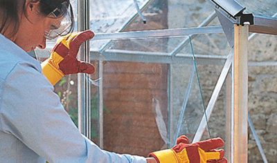 Person wearing gloves and eye protection slotting a section of glass into a greenhouse frame.