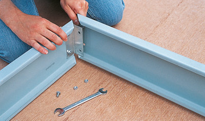 Person fitting two sections of a steel greenhouse base together in the corner.