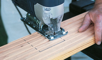 Using a jigsaw to cut out a square notch which has been marked on a decking board to show the location of deck posts.