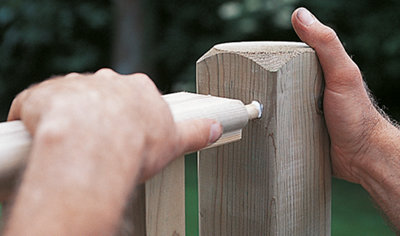 Person slotting the wooden dowels at the end of a decking balustrade into two holes that have been drilled in a decking post to secure the balustrade in place.