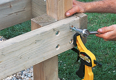 Using a ratcheting socket spanner to drive a coach screw through a decking subframe into a deck post, which is clamped to the inside of the subframe.