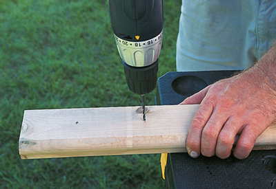 Using a drill to drill a pilot hole in a piece of timber sat on a workbench.