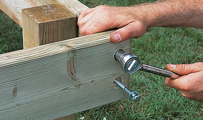 Person using a ratcheting socket wrench to tighten coach screws, securing two pieces of timber together at the corner of a deck frame.