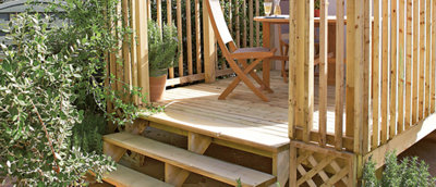 A small raised timber deck featuring wooden steps, a railing, and a small table with chairs on top, creating a cozy outdoor seating area.
