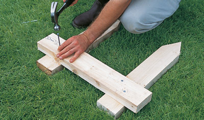 A person hammering a nail into a piece of timber, which stretches across two timber stakes, creating a timber profile.