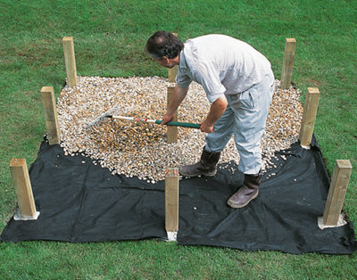 Spreading gravel over the top of a weed control membrane that has been laid around the deck joist support posts.
