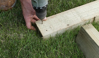 A person using a drill to create a pilot hole in a piece of timber.