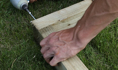 A person using a drill to drive a screw through two pieces of timber, securing them together at a corner joint.