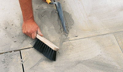Person using a trowel to push mortar into the joint between two paving slabs.