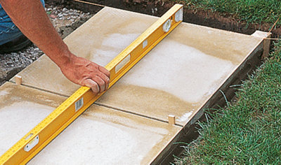 A person holding a spirit level across two paving slabs to check that the surface is flat and level.