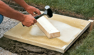 A person hitting a piece of timber resting on top of a paving slab with a hammer to ensure the slab is level.