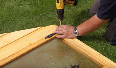 Using a drill to attach the hinge for a playhouse door onto the playhouse frame.