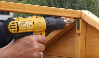 Using a drill to secure an angle bracket to a playhouse frame and roof support.
