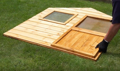 A person wearing gloves laying the front panel of a wooden playhouse on the ground.