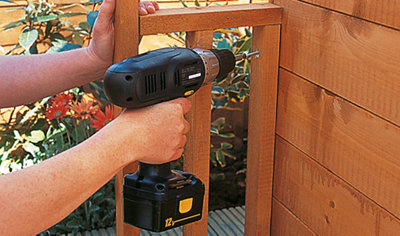 Using a drill to secure the wooden veranda rails to the front of a wooden playhouse.