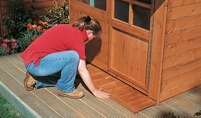 Person positioning a playhouse veranda floor in front of a completed playhouse.