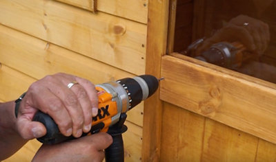 Using a drill to create a pilot hole in the door of a playhouse.