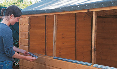Person lining up a metal windowsill with a shed window opening.