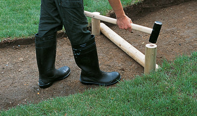 Using a sledgehammer to knock timber logs into the ground to support a step riser.