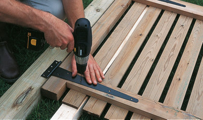 Person using a drill to drill pilot holes through the holes on a gate hinge into the gate.