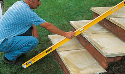 A person holding a long spirit level across the treads of three garden steps to check they're in line.