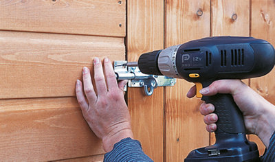 Person using a drill to secure a sliding bolt lock to the outside of a shed.