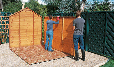 Two people lining up a shed side panel against a back panel which has already been installed.