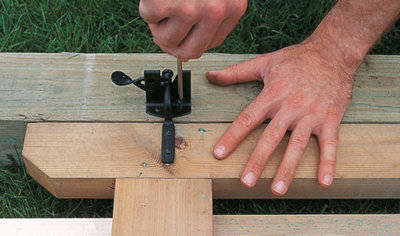 Person using a screwdriver to secure a gate latch to a gate post with a screw.