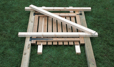 Three timber lengths placed on top of a gate and gate posts for support. Two timber lengths are positioned horizontally, while the third is placed diagonally between them.