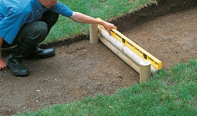 Using a spirit level to check that a timber log step, comprised of two logs and two supports, is level.