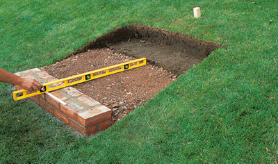 Using a spirit level to check that the hardcore laid behind a course of bricks rises slightly towards the back.