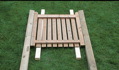 A gate laid on the ground between two gate posts, resting on two timber lengths to align it with the gate posts.