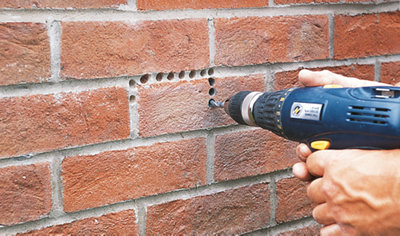 A person using a drill to make multiple 10mm holes in a brick wall.