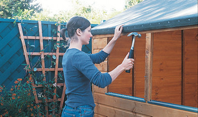 Person using a hammer to secure wood window cloaks to the window opening of a shed.