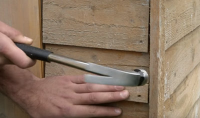 Using a hammer to drive a loose nail into the outside of a shed.