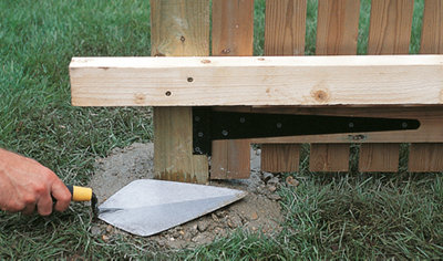 Using a trowel to shape concrete around the base of a gate post, sloping it away to aid water runoff.