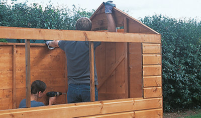 Person using a drill to secure a shed side panel to the back panel, whilst someone else holds the two panels in place.