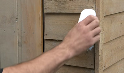 Using a cleaning cloth to wipe down the exterior of a garden shed.