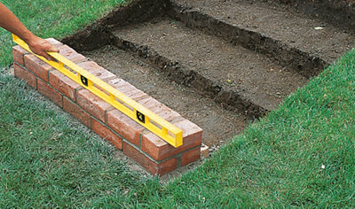 A person using a spirit level to check that a course of bricks, laid in stretcher bond pattern, is level.