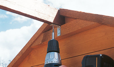 Using a drill to secure an L bracket which is joining the shed back panel to the roof support beam.