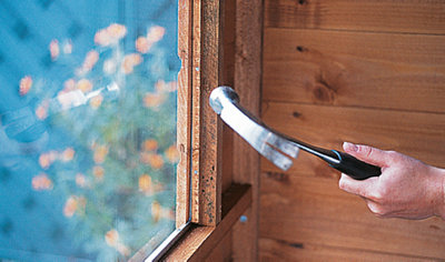 Person using a hammer to secure the window beading to the edge of a shed window inside the shed.