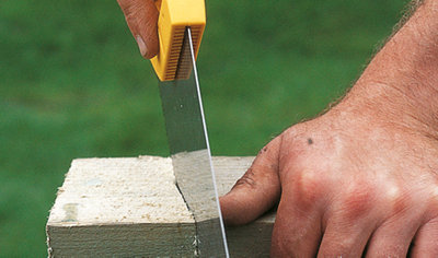 Person using a saw to cut along a marked line on a gate post.