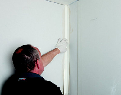 A person pressing a plasterboard angle bead into jointing compound that has been applied to the corner joint of two plasterboard walls.