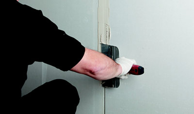 A person using a filling knife to apply jointing compound to cover the join between two sheets of plasterboard on a plasterboard wall.