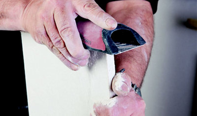 A person running a plasterboard rasp along the edge of a sheet of plasterboard that has been cut, to neaten up the edges.