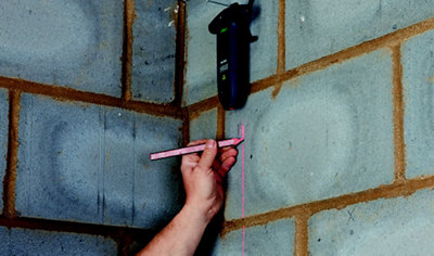 A person using a laser level mounted on the wall to draw a vertical line, marking where the first plasterboard of a dry lining project will be installed.