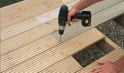 Using a drill to secure a deck board to a deck joist, with the board positioned halfway across the joist.