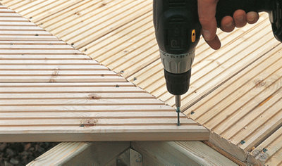 Using a drill and decking screw to secure a deck board, cut at a 45-degree angle, to a deck joist.