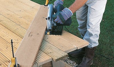 Person using a circular saw to cut a corner out of a deck, with the saw running along a piece of timber clamped to the deck as a guide.