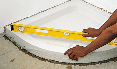 Person holding a spirit level over the top of a shower tray which has been installed on a bed of mortar.